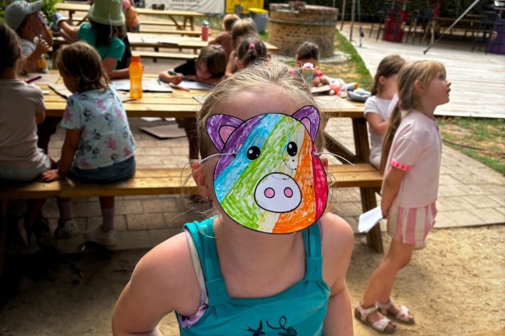 Kind met een zelfgeknutseld varkensmasker aan de picknicktafel